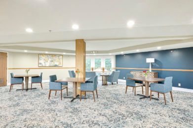 A modern seating area with tables and chairs, featuring carpeted flooring and stylish lighting.