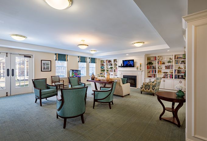 A spacious and well-lit living room with comfortable seating, tables, a fireplace, bookshelves, and a television.