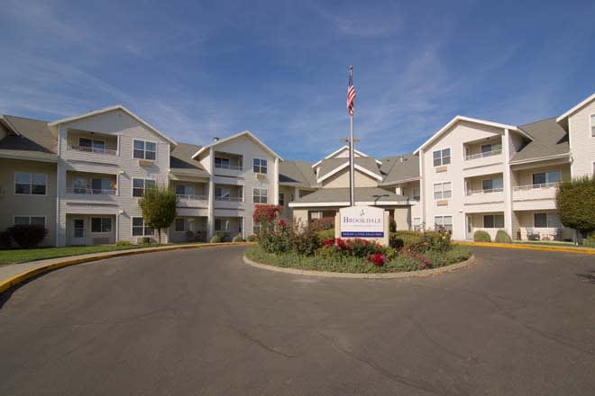 A residential apartment complex with multiple buildings and a circular driveway under a clear blue sky.