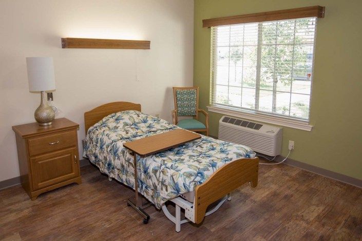 A hospital room featuring a single bed, bedside table, and large window.