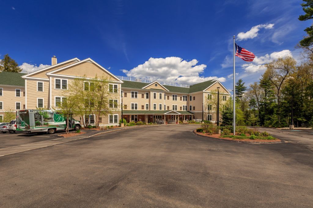 A multi-story residential building with an American flag in the foreground, set against a clear blue sky.