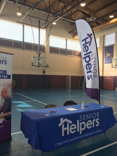 A setup for Senior Helpers at a gymnasium featuring a table and promotional banner.
