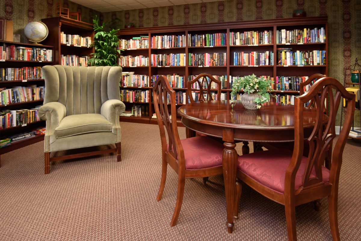 A cozy library corner with bookshelves, an armchair, and a round table with chairs.