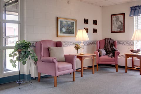 A cozy living room with two pink armchairs, a lamp, and wall decor.