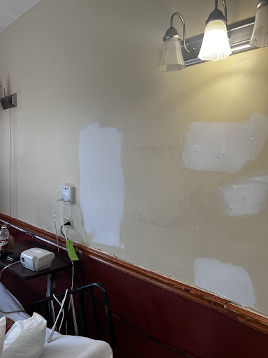 A partially painted wall showing patches of white paint over a beige background, indicating ongoing renovation work.