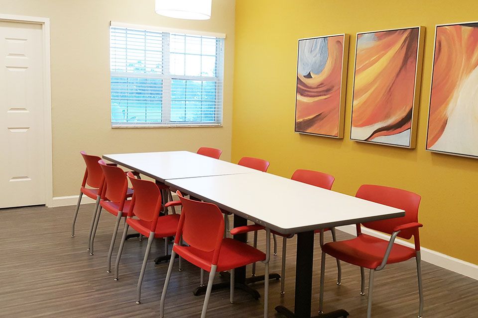 A bright conference room with a long table and vibrant orange chairs against yellow walls.