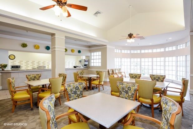 A bright and spacious dining area with multiple tables, chairs, ceiling fans, and large windows.