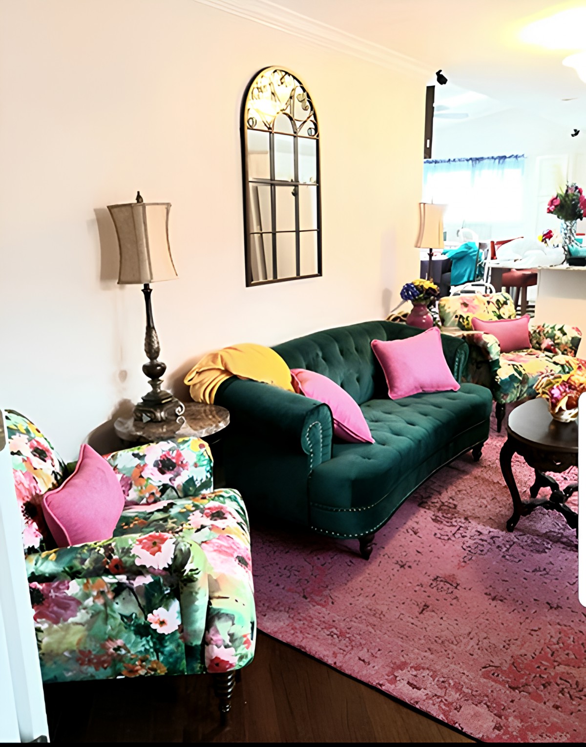 A cozy living room with a green sofa, floral chairs, and pink accents.