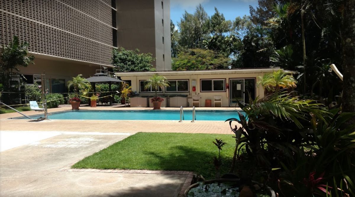 A serene outdoor swimming pool area surrounded by green plants and buildings.