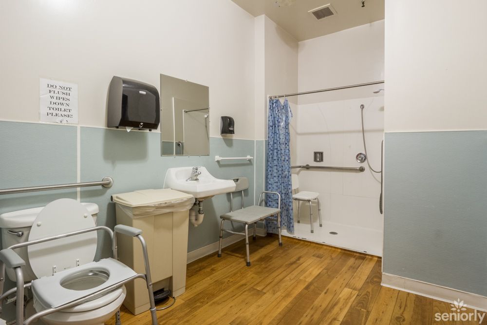 A wheelchair-accessible bathroom featuring grab bars, a shower chair, and a sink.