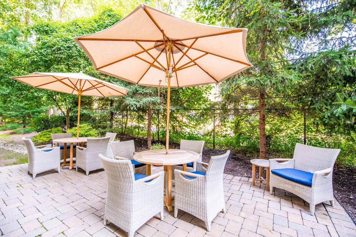 A cozy outdoor patio area with tables and umbrellas surrounded by lush greenery.