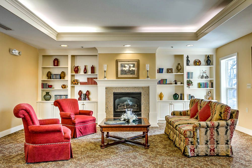 A cozy living room with a fireplace, red chairs, and a patterned sofa surrounded by built-in bookshelves.