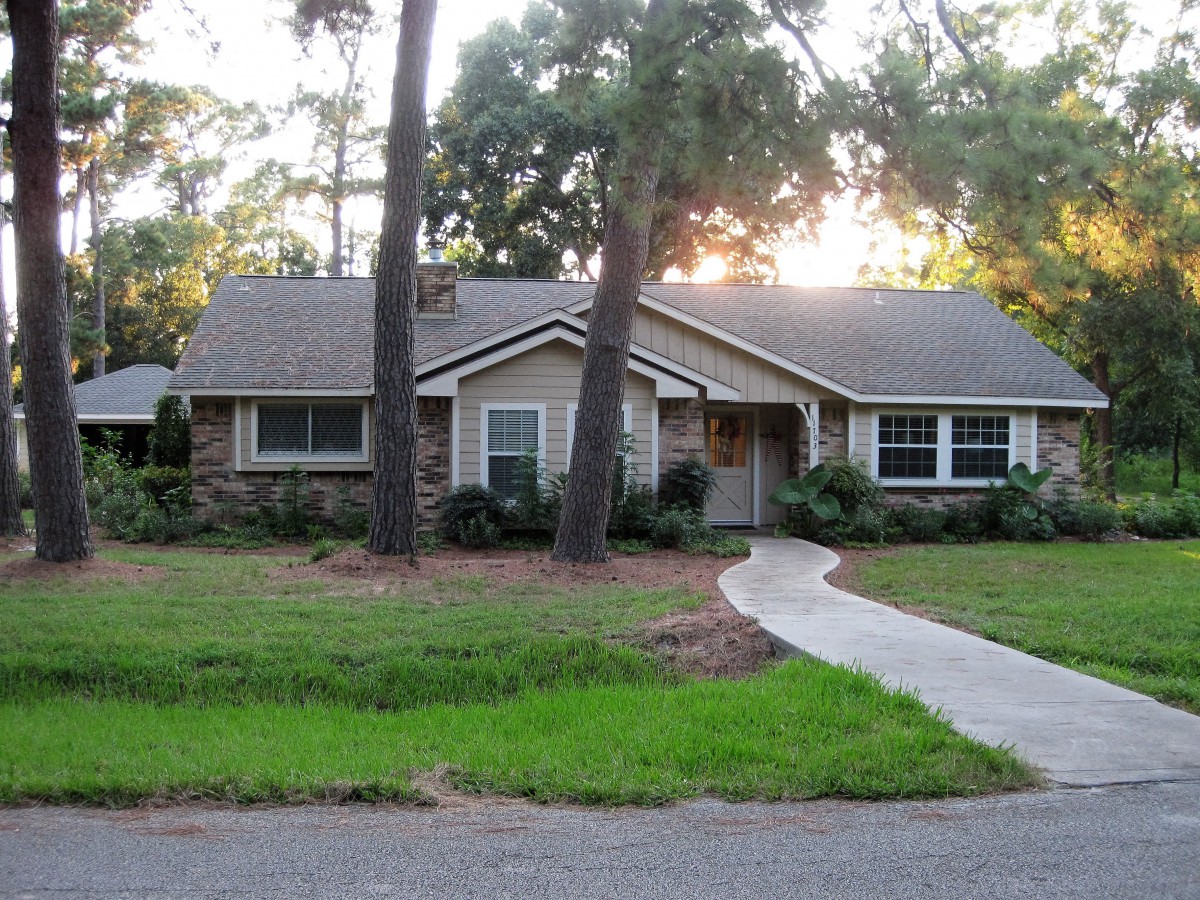 A suburban house surrounded by trees with a neatly maintained lawn and pathway.