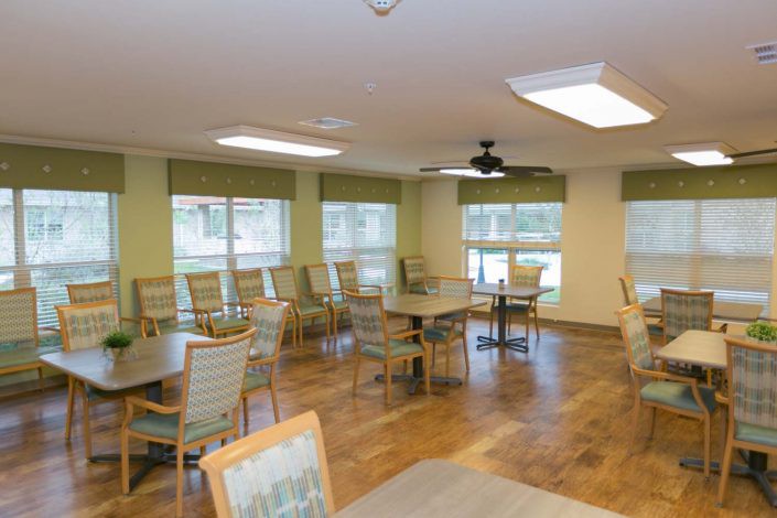 A spacious dining area with multiple tables and chairs, large windows, and wooden flooring.