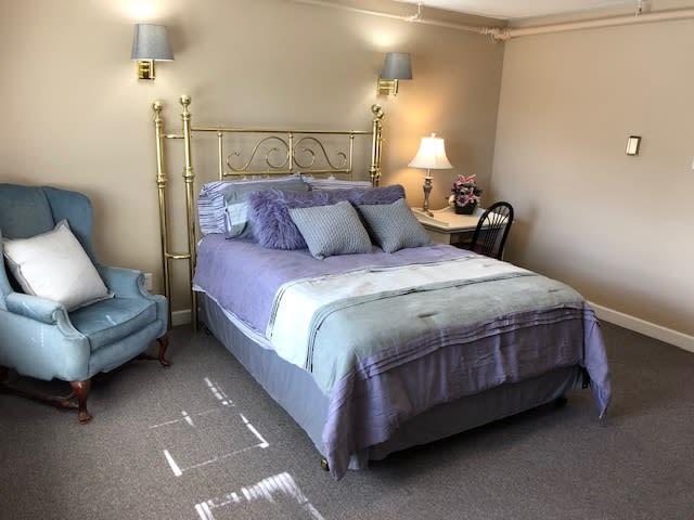 A cozy bedroom with a neatly made bed, an armchair, and a bedside table lamp.