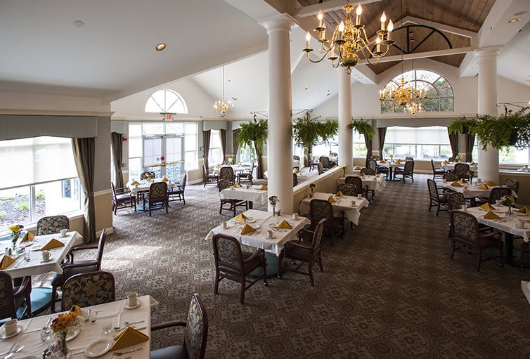 A spacious and elegant dining area with chandeliers, natural lighting, and neatly arranged tables and chairs.