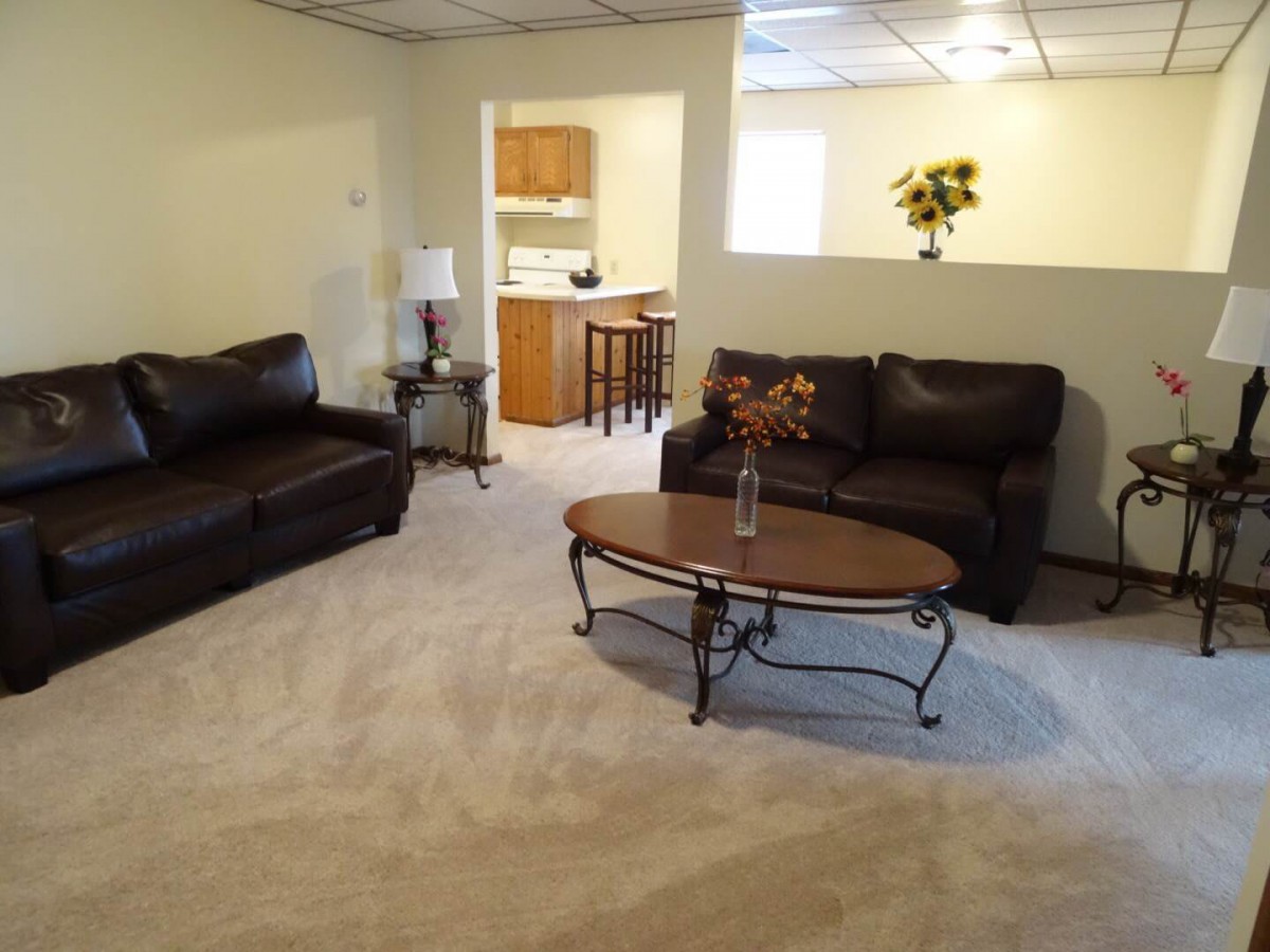 A cozy living room with dark sofas, a wooden coffee table, and a view into the kitchen.