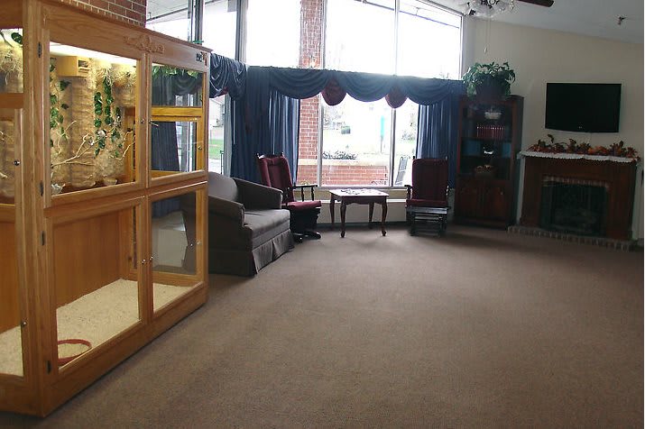 A spacious lobby area featuring chairs, an aquarium, large windows with curtains, and a carpeted floor.