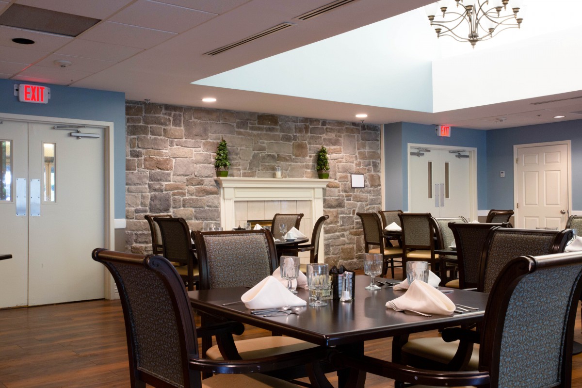 An elegant dining room with neatly set tables and a stone wall featuring a fireplace.
