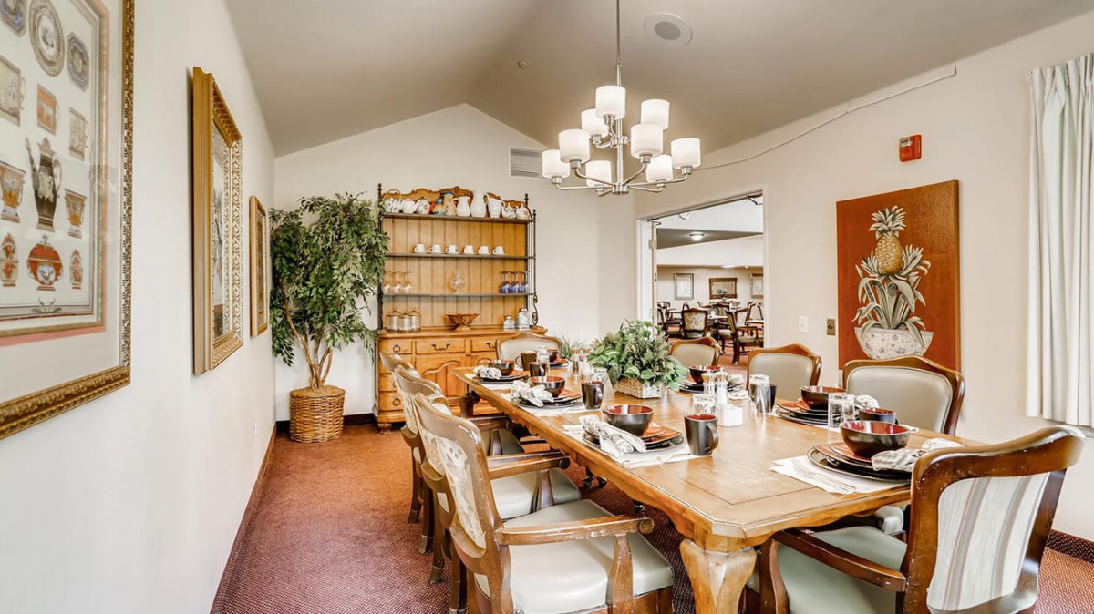 A cozy dining room with a large wooden table and elegant chairs, adorned with a chandelier and surrounded by tasteful decor and plants.