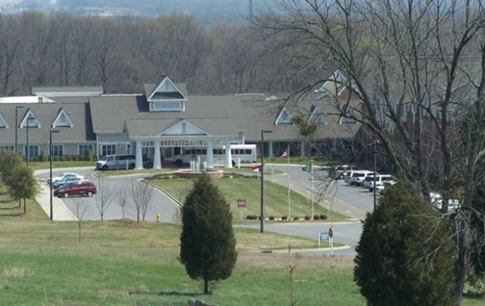 A building with a driveway, surrounded by trees and a parking lot.