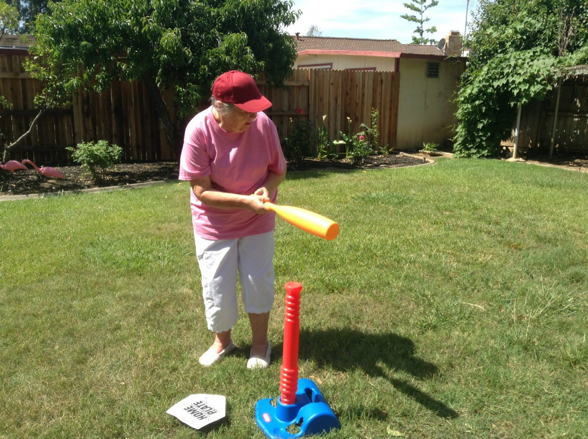 A person playing tee ball in the backyard, preparing to hit a ball with a plastic bat.