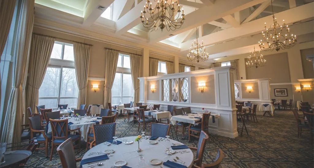 An elegant dining room with chandeliers, large windows, and neatly set tables.