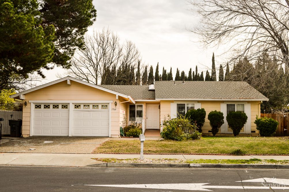 A suburban house with a front yard and attached garage, set against a backdrop of tall trees.