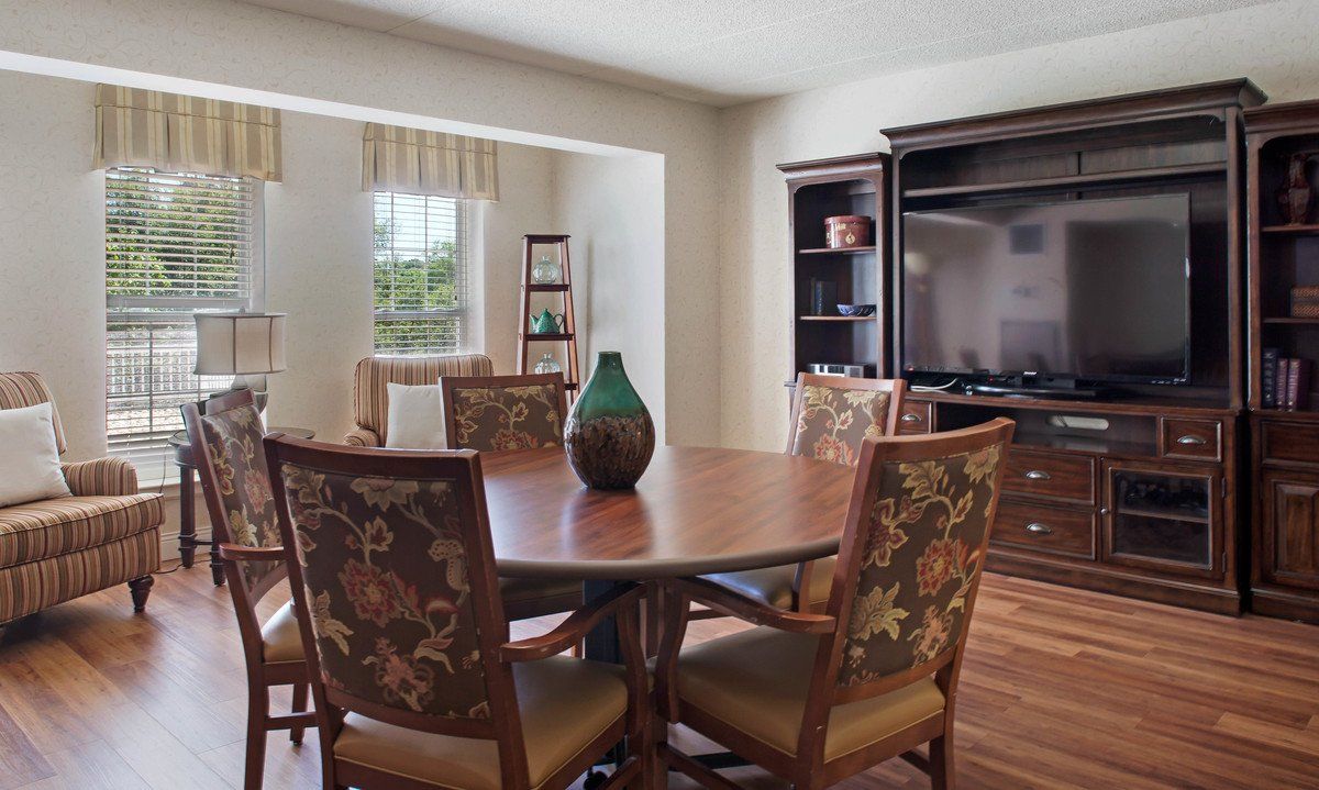 A cozy dining area with a wooden table and floral chairs, adjacent to a living room space with an entertainment center.