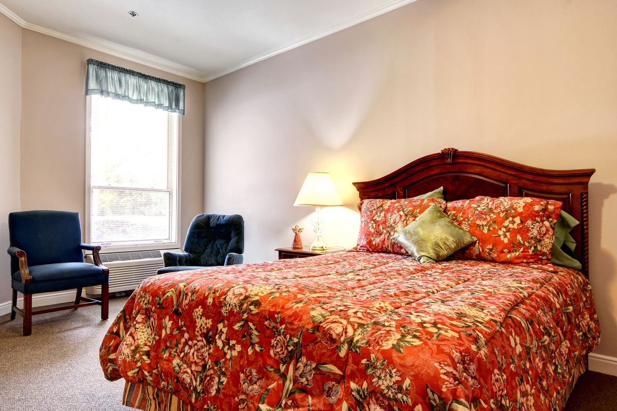 A cozy hotel room featuring a bed with floral bedding, a lamp, and a chair by the window.