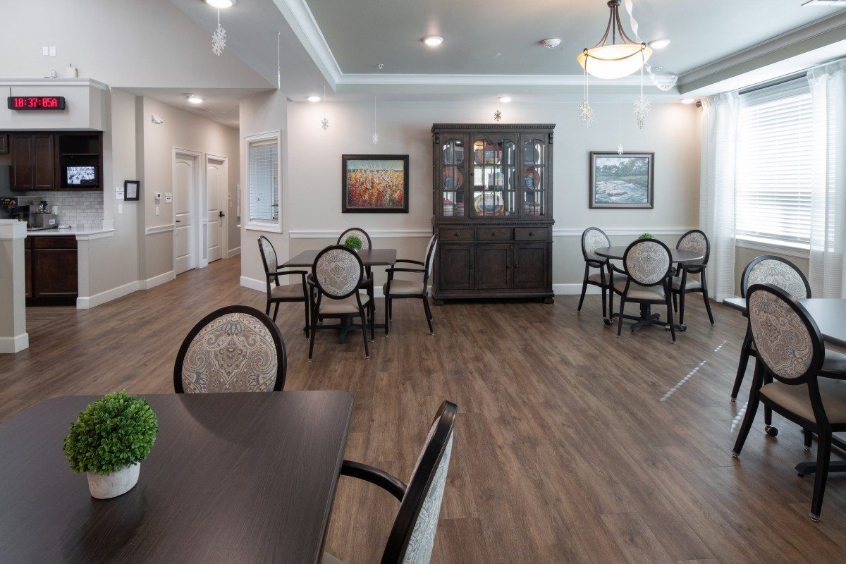A spacious dining area featuring round tables, chairs, a cabinet, and soft lighting.