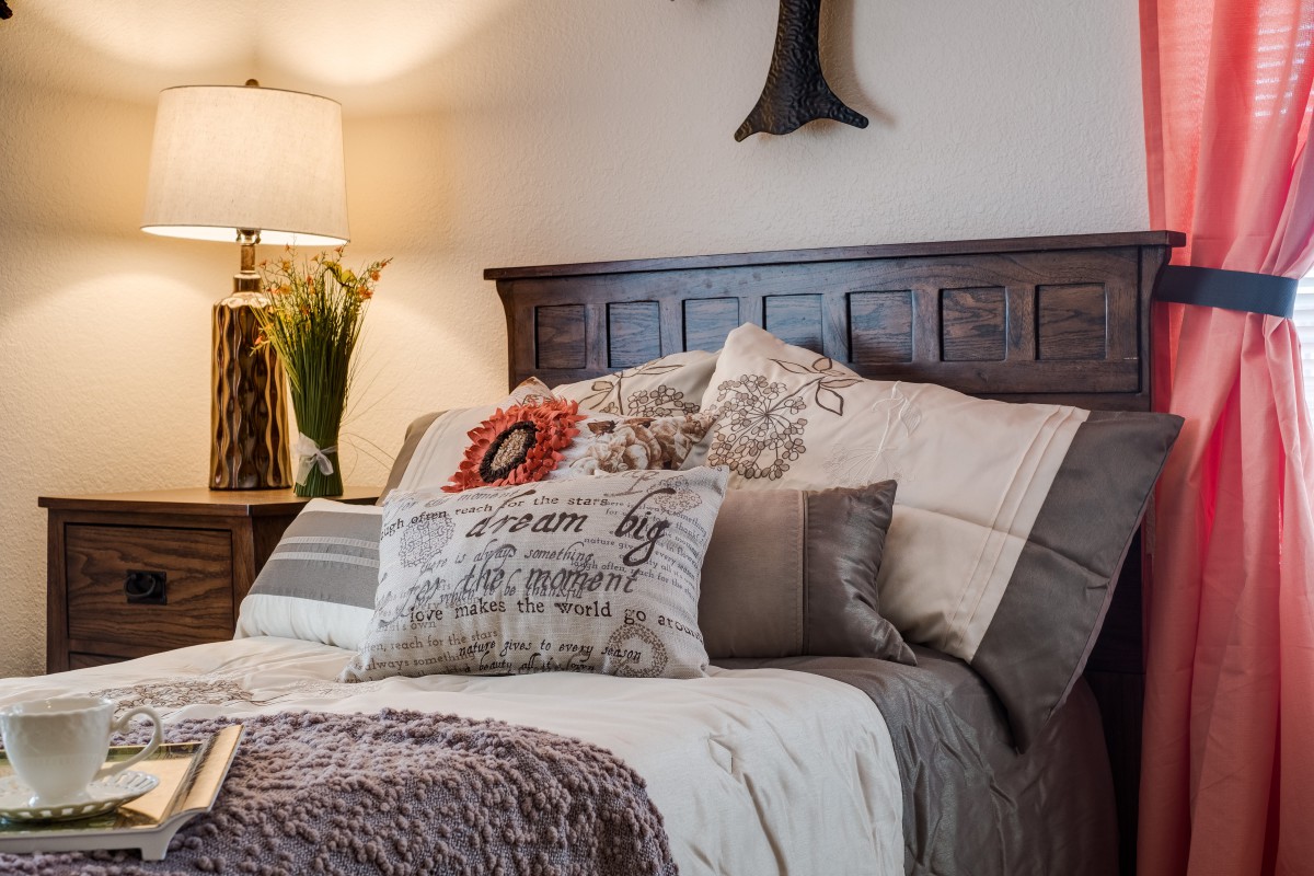 A cozy bedroom with a wooden headboard, decorative pillows, and soft lighting.
