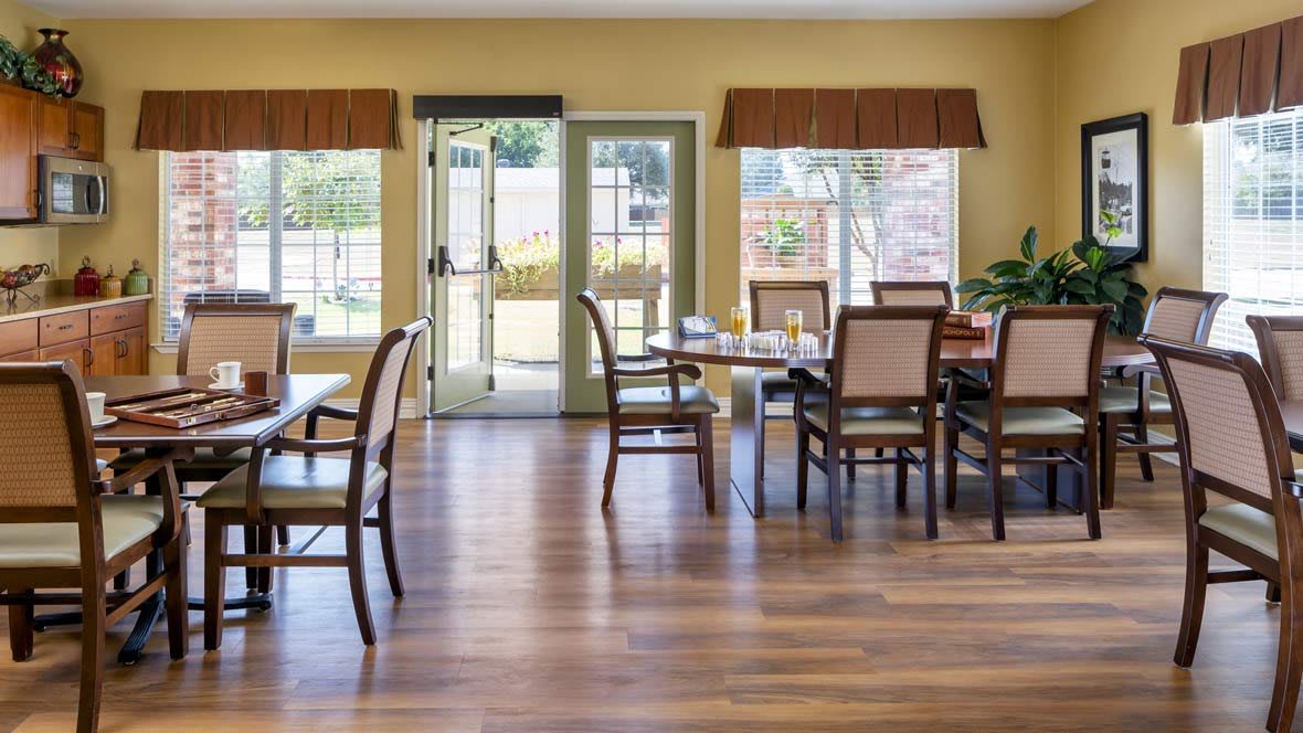 A well-lit dining room with several tables and chairs arranged on a wooden floor.