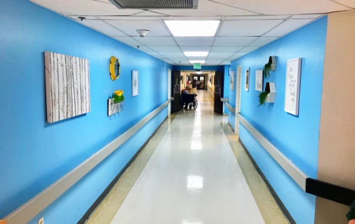 A brightly lit hospital corridor with blue walls and artwork.