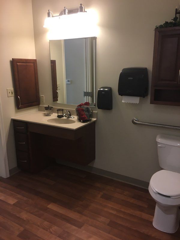 A bathroom with a vanity, mirror, toilet, and dispensers.