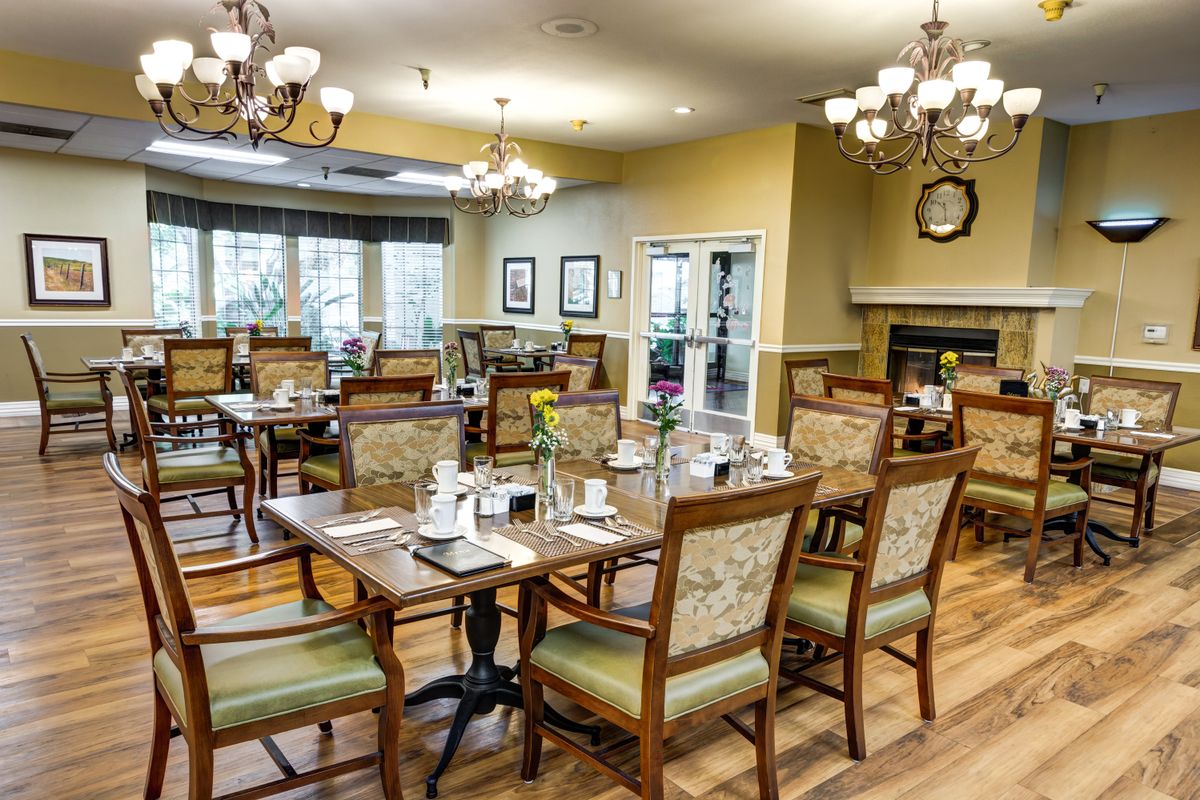 An elegantly decorated dining room with multiple tables and chairs, featuring chandeliers and wooden flooring.