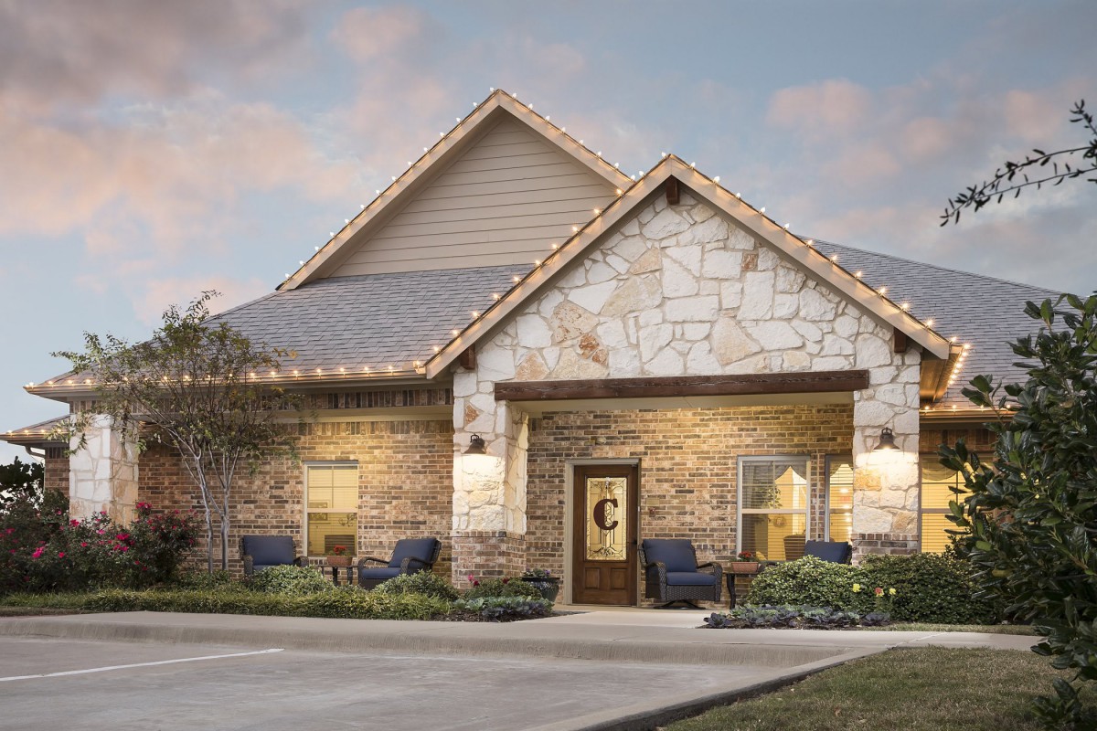 A well-lit stone house with a welcoming exterior and landscaped surroundings during the evening.