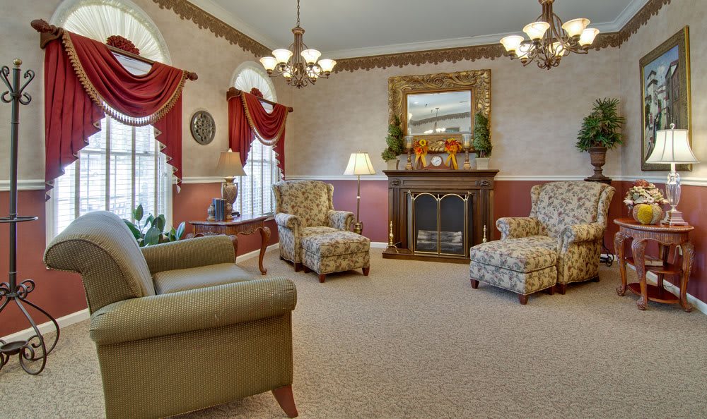 A traditional living room with elegant decor featuring a fireplace, armchairs, chandeliers, and draped windows.