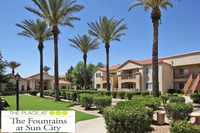 A well-maintained apartment complex with palm trees and manicured landscaping under a clear blue sky.