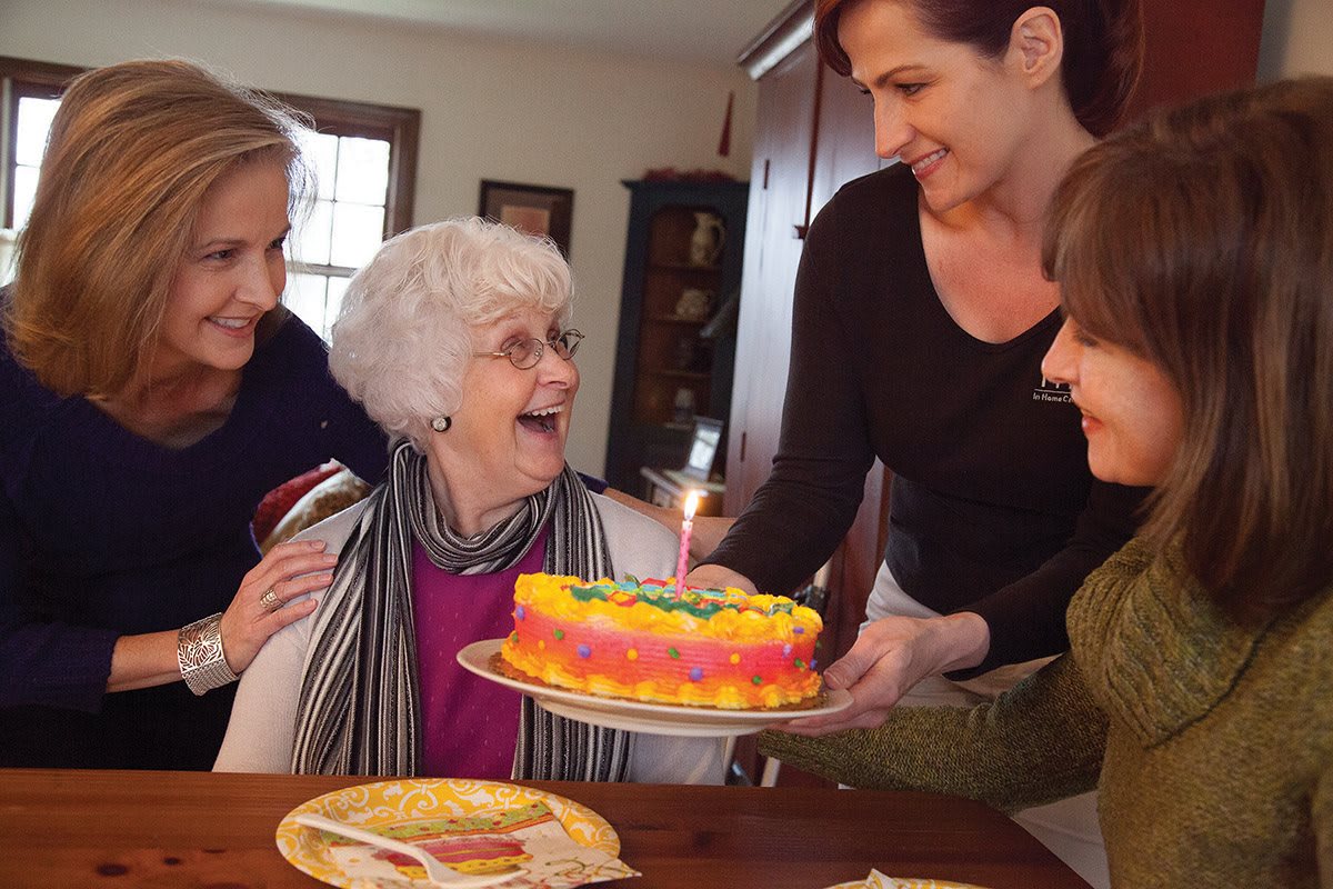 An elderly woman joyfully celebrating her birthday with family around a colorful cake.