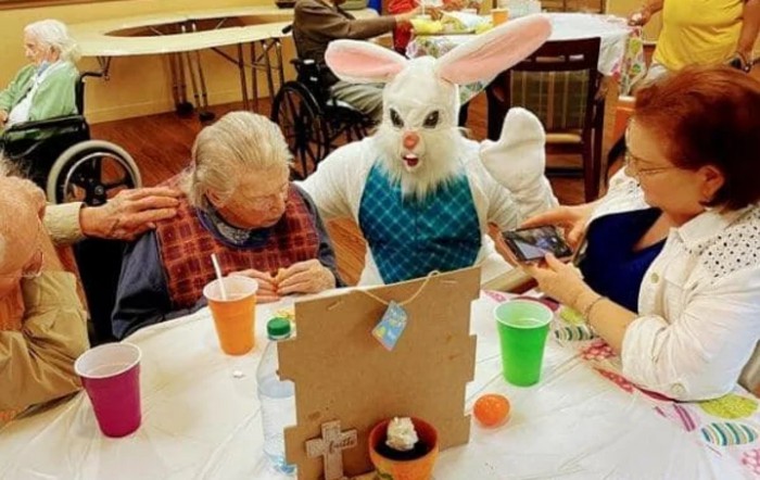 An Easter Bunny entertains an elderly person at a festive indoor event.