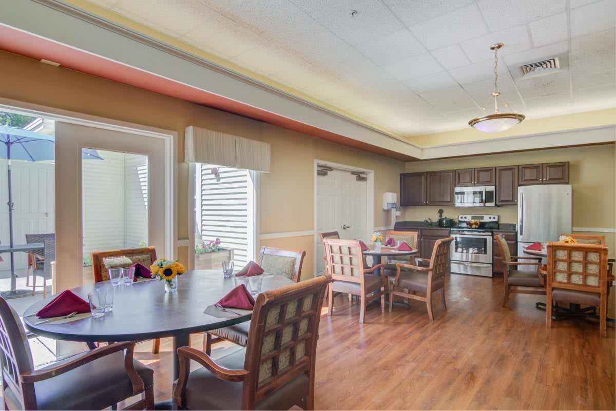 A dining area with multiple tables and chairs, adjacent to a kitchen with modern appliances.