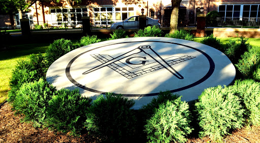 A prominent Masonic symbol featuring the square and compasses set against a background of greenery.