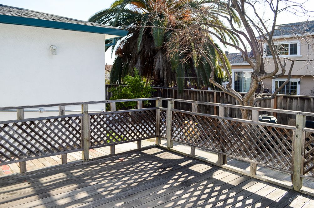 A sunny outdoor deck with wooden railings and a view of palm trees.