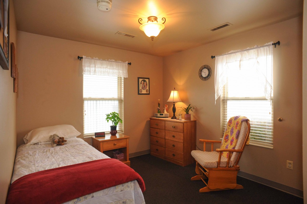 A cozy bedroom with a rocking chair, dresser, and a warmly lit lamp.