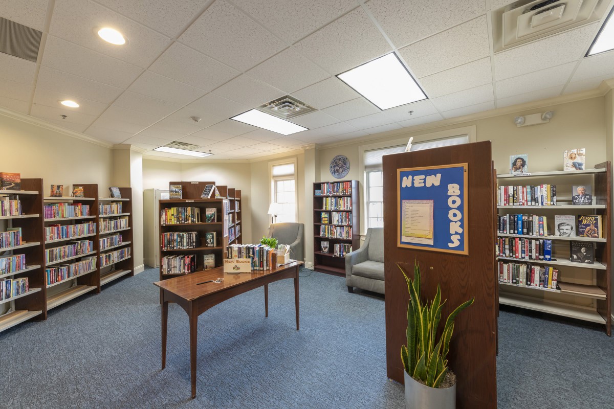 A cozy library interior with shelves of books, a table displaying new releases, and comfortable seating.