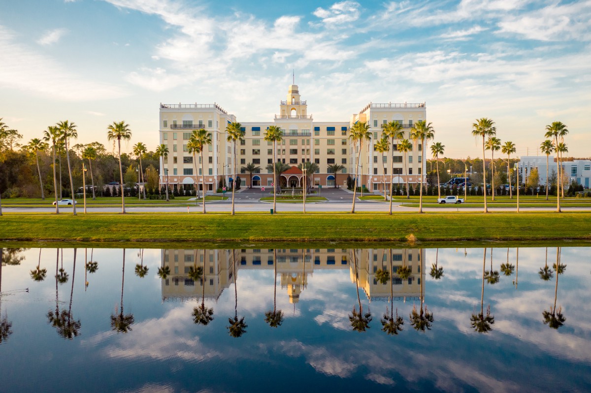 A grand building with palm trees and its reflection in a body of water under a blue sky.