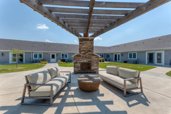 A cozy outdoor patio with a pergola, featuring comfortable seating and a stone fireplace.
