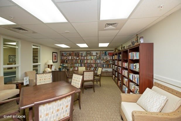 A cozy library room with bookshelves, tables, and chairs for reading.
