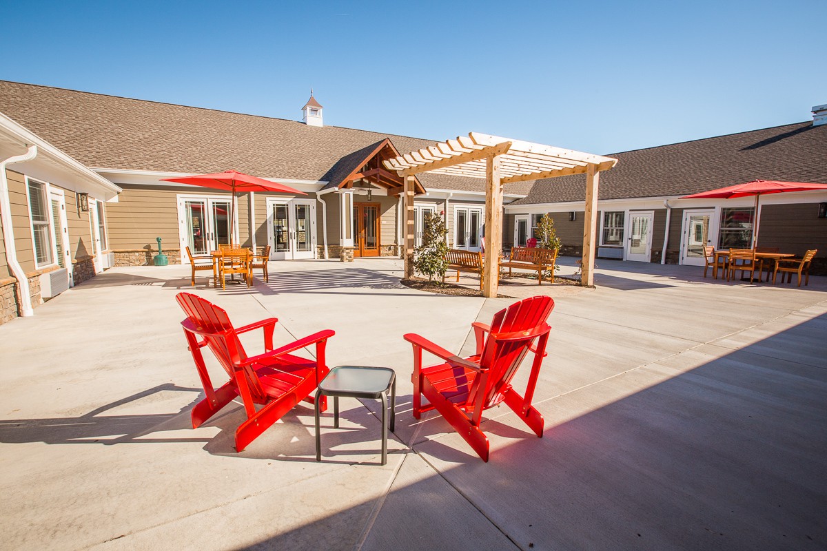 A sunny patio area with red chairs and a pergola.
